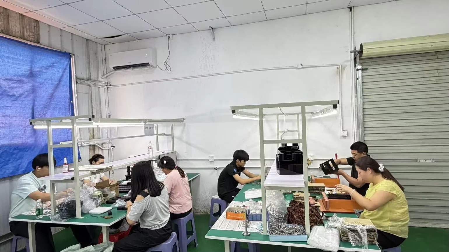 Chengshuo team members handling parts at illuminated workbenches in a supplier-assessment photograph.